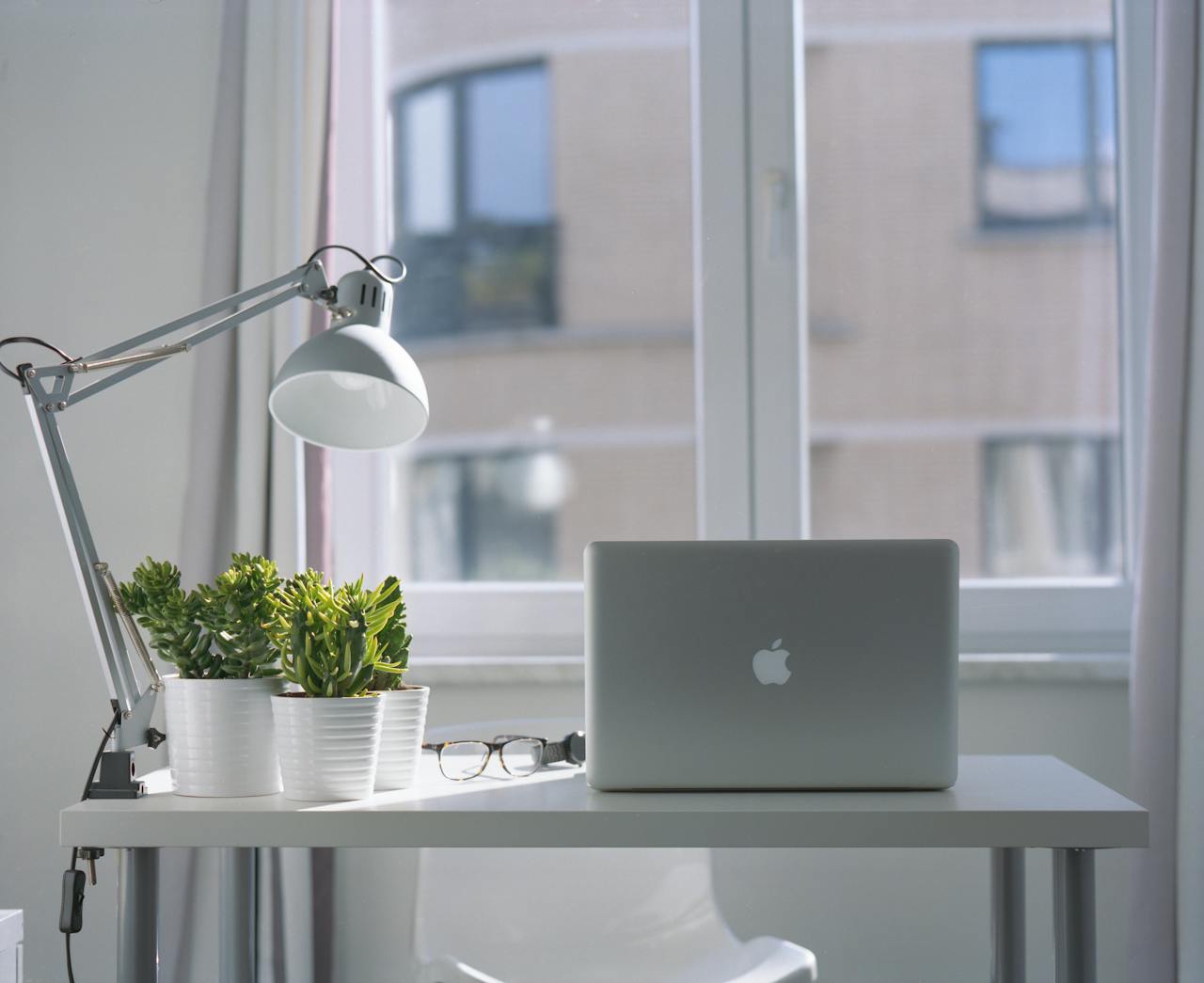 Services Bright modern workspace with laptop, potted plants, and desk lamp near a window.